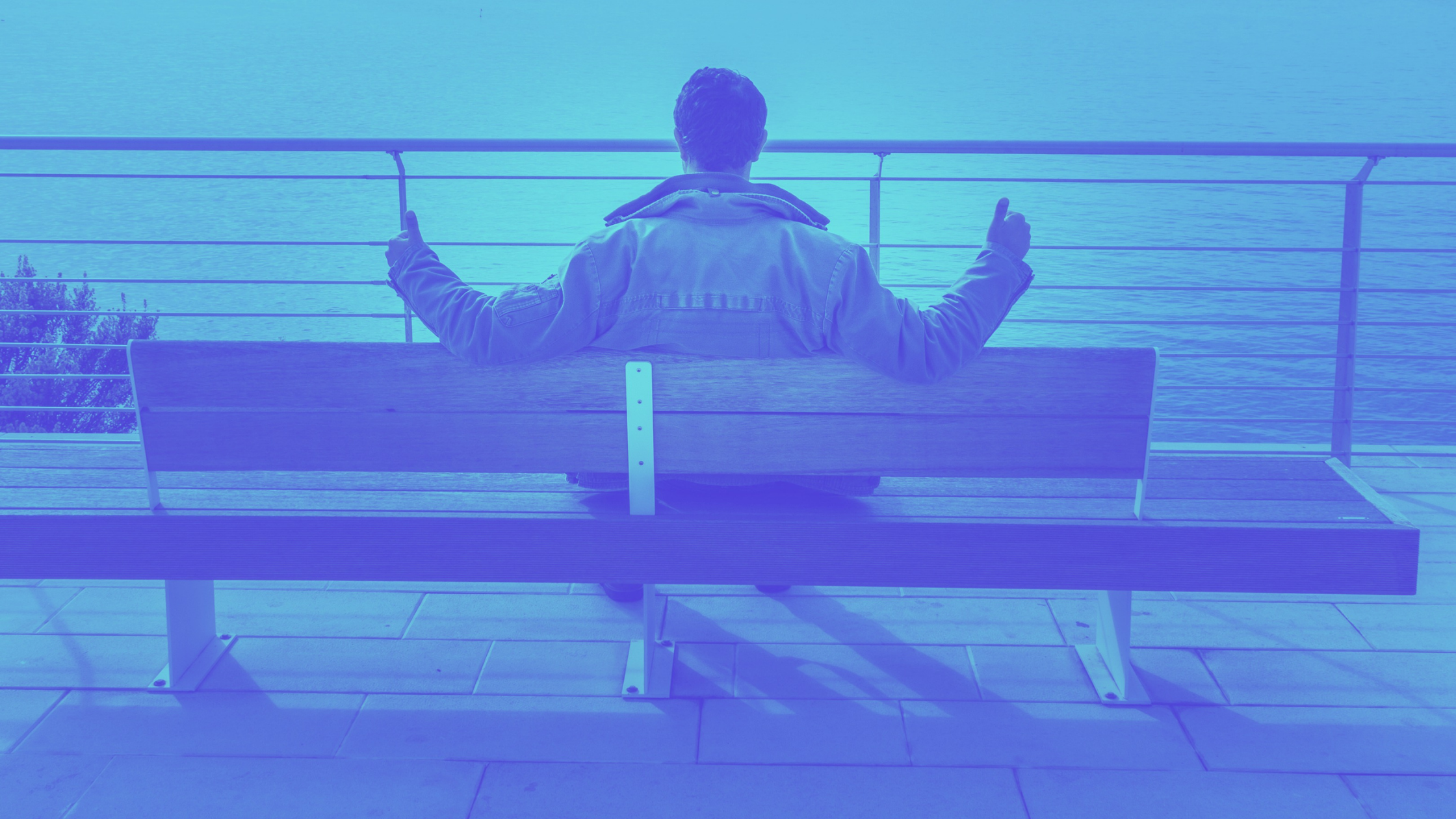 Man sitting on bench looking at water with 2 thumbs up